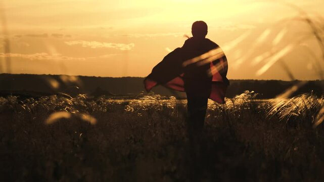 Sunset silhouette of a young dreamer, A child's adventure in the countryside, Running with the wind and chasing dreams, The golden fields of imagination, The playful spirit of a free soul, Superhero