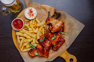 Appetizing fried wings with french fries sauce and beer on a wooden board. view from above