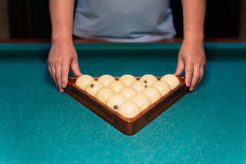 Player arranging billiard balls in triangle on green pool table. Man playing snooker.
