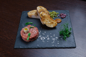 Beef tartare. Cold appetizer of raw marinated meat with quail egg, herbs and spices on a ceramic tray and wooden table. side view