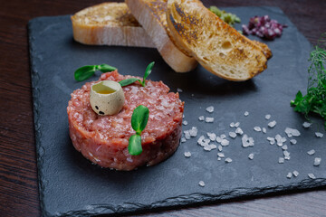 Beef tartare. Cold appetizer of raw marinated meat with quail egg, herbs and spices on a ceramic tray and wooden table. snack in the restaurant