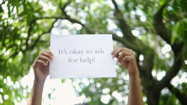 Person holding sign asking for help under a tree