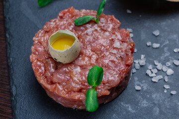 Beef tartare. Cold appetizer of raw marinated meat with quail egg, herbs and spices on a ceramic tray and wooden table. snack in the restaurant. beautiful presentation. meat with egg close up