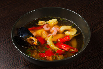 Appetizing looking seafood soup with mussels shrimp red pepper in a plate on a wooden table. fresh seafood