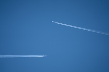 a pair of twin engined jet liner aircraft with contrails, passing at high altitude, clear blue sky
