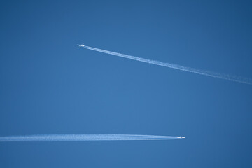 a pair of twin engined jet liner aircraft with contrails, passing at high altitude, clear blue sky
