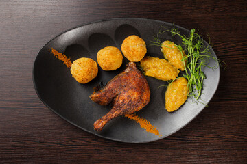 Very healthy roast duck thigh with potatoes and greens on a black plate on a wooden table serving in a restaurant. nice decoration of the dish. view from above