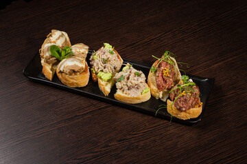 Three types of bruschetta on a table on a black plate beautiful serving in a restaurant