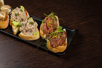 Three types of bruschetta on the table on a black plate beautiful serving in a restaurant. side view