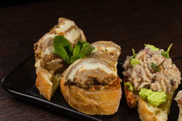 Three types of bruschetta on the table on a black plate beautiful serving in a restaurant. classic snack. close-up of bruschetta with pate and butter