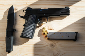 A classic American pistol 45 caliber and a tactical knife on a wooden surface under the rays of the...