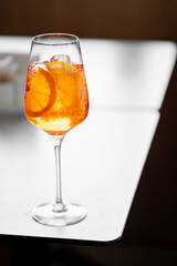 A vibrant Aperol Spritz cocktail in a glass with orange slices and ice, placed on a sleek white table, showcasing a minimalist and refreshing aesthetic.