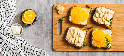Sandwiches with ricotta, orange and banana on a board on a table top view web banner