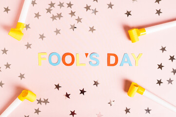 April Fools' Day written in colored letters, whistles, stars and tulips on pink top view