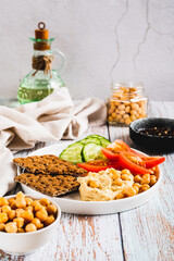 Hummus, chickpeas, tomato, cucumber, grain crackers on a plate on the table vertical view