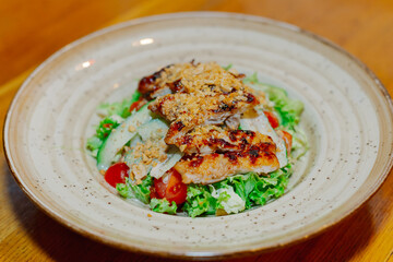 Fresh salad of vegetables with pieces of chicken grilled upstairs in a plate on a wooden table in a cafe. close-up