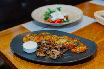 A plate with fried pancakes of potatoes fried meat with onions and sauce on a wooden table. The kitchen of the whole world. Beautiful food feed. tasty food