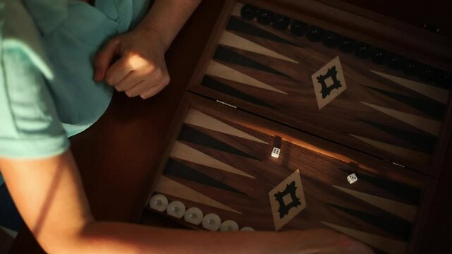 A close-up of a backgammon game in progress, showing the game board, dice, and a hand making a move. The person&rsquo;s hand is poised, highlighting a moment of strategy in a competitive game.