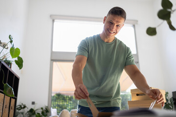 Man unpacking cardboard boxes in new home smiling at camera