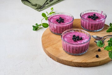 Berry dessert, yogurt mousse or jelly with blueberries in glass bowls on a wooden board on a light concrete background. No-bake desserts.