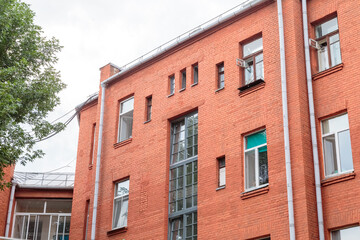 The facade of the old red brick building that was built 100 years ago against the backdrop of the White Sky. Ancient decoration of the building. Restoration of buildings. Old details. Large windows on