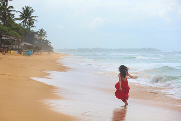 Girl in long red dress running on the beach in the morning. Soft focus
