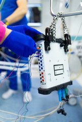 Hospital med equipment tweaks. A healthcare professional in blue scrubs operates medical equipment with multiple wires in a hospital environment.