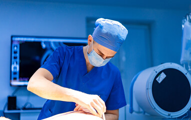 Surgeon readying for surgery. A surgeon in blue scrubs and mask performs a procedure in a well-lit...