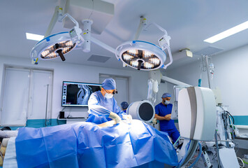 Surgeon at work in hospital. A surgeon operates on a patient under bright lights in a high-tech...