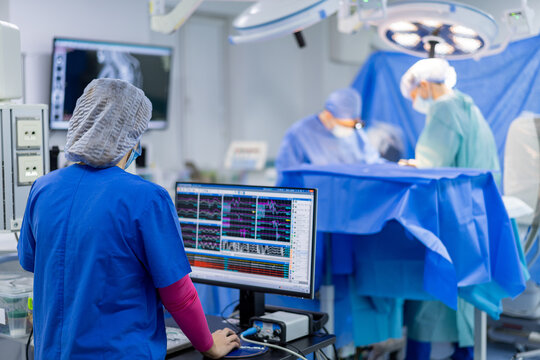 Surgeon operating in modern hospital. Surgeons monitor vital signs on a computer during an operation in the hospital's operating room.