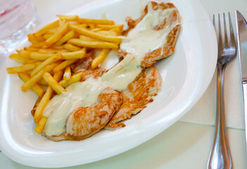 Appetizing carve pork topped with piquant creamy sauce and French fried potato