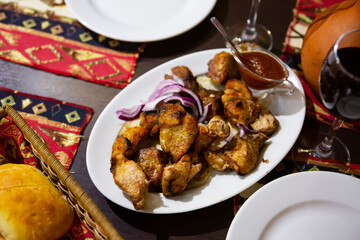 Georgian traditional food, fried pork shashlik on a ceramic plate with onions and sauce