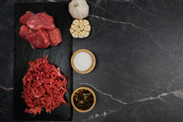 Top view of chunks of beef meat and red minced meat with streaks of fat lying on a black background...