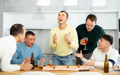 Friends drinking beer and enthusiastically playing a board game at home
