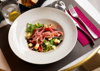 Light dish of arugula salad with mushrooms, ham and cheese on table in restaurant