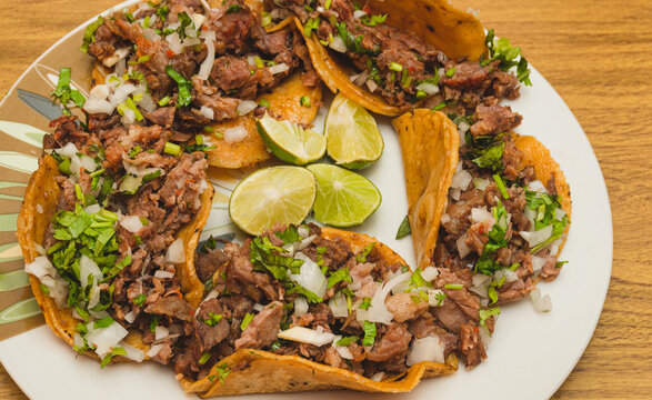Tacos de suadero con cilantro y cebolla acompa&ntilde;ado con limones en el centro sobre un plato blanco