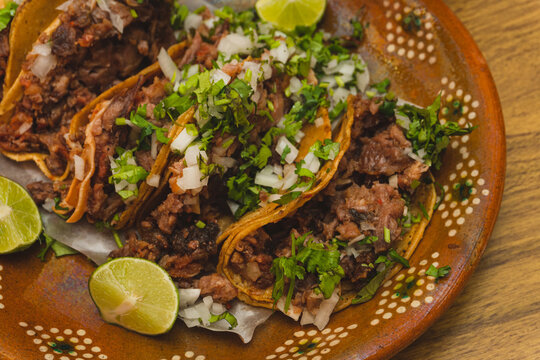 Tacos de suadero con cilantro y cebolla acompa&ntilde;ado con limones sobre un plato de barro