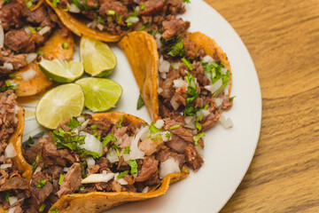 Tacos de suadero con cilantro y cebolla acompañado con limones en el centro sobre un plato blanco