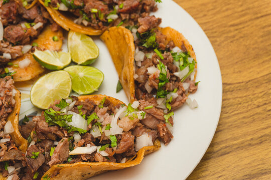 Tacos de suadero con cilantro y cebolla acompa&ntilde;ado con limones en el centro sobre un plato blanco