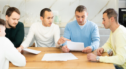 Friends reading financial documents and trying to solve problems together while sitting at table in their home kitchen