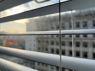 Close-up of slatted Venetian window blinds with blurry cityscape in the background