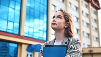 Professional businesswoman reviewing documents, standing near sleek skyscraper, representing...