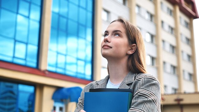 Professional businesswoman reviewing documents, standing near sleek skyscraper, representing corporate ambition and leadership potential