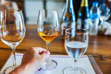 Close-up view of hand holding wine glass on tasting table with water glass and wine bottles in background. Mexico.
