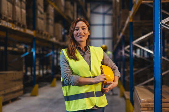 Confident Female Worker Holding Safety Hard Hat in Warehouse Setting