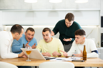 Group of male friends solving problems using laptop and drinking beer at home