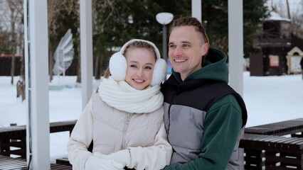 Obraz premium Winter clad couple hugging in snow dusted gazebo, sharing warm smiles amid frosty landscape, radiating romantic connection during peaceful seasonal moment