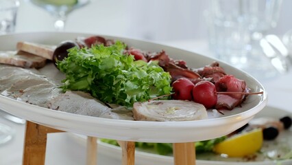 Sliced deli meats arranged with crusty bread roll, endive leaves, and vibrant red berries on white oval platter, showcasing rustic culinary composition