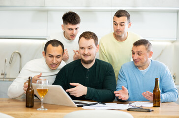 Group of football fans drinking beer and watching football match on a laptop at home