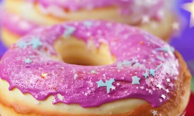 A tall stack of fluffy donuts drips with frosting that slowly shifts colors between pink, blue, and gold. Tiny edible stars sparkle on the surface. Close-up shot. Fantasy food aesthetic - Powered by Adobe